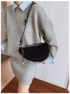 Detail of black suede crescent bag with knotted strap and gold hardware on model