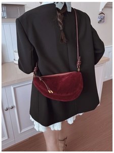 Detail of burgundy suede half-moon bag featuring a unique knotted shoulder strap design