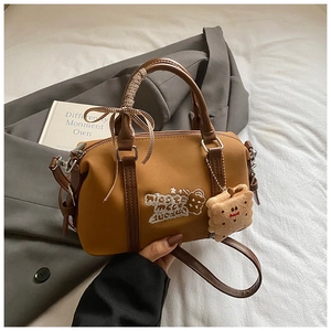 Close-up of brown Boston bag with cartoon patches and a plush cookie pendant detail