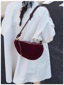 Deep burgundy suede crescent bag with knot detail and gold zipper shown on model