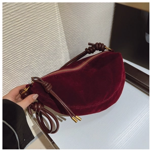 Macro shot of burgundy faux suede crescent bag with knotted strap and gold zipper