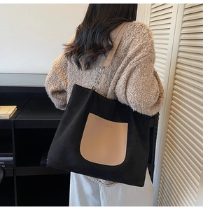 Detail view of large black canvas tote bag with camel leather pocket and wide strap