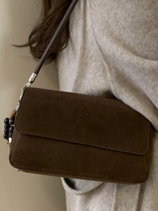 Minimalist dark brown suede shoulder bag with bead charm shown on a beige sweater