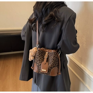 Detail of leopard print bucket bag featuring brown leather trim and a cute teddy bear charm