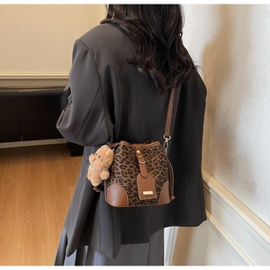 Detail view of leopard print bucket bag with plush bear charm worn by a model
