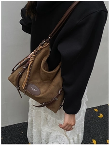 Detail view of brown faux suede hobo bag with woven tassel and decorative strap charms