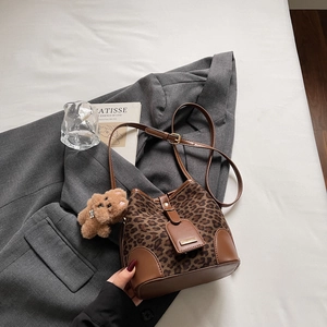 Detail of leopard print bucket bag with brown leather accents and a cute plush bear charm
