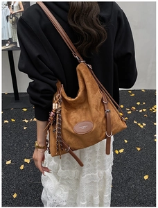Detail of dark brown suede tote bag with leather logo patch and braided tassel charm