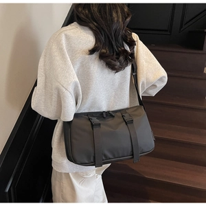 Side view of a large black nylon crossbody messenger bag on a model in urban setting