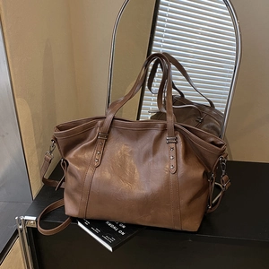 Large dark brown faux leather tote bag with star studs and adjustable strap displayed on a desk