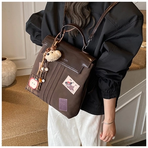 Detail of vintage brown college backpack with patches and white fluffy ball pendant