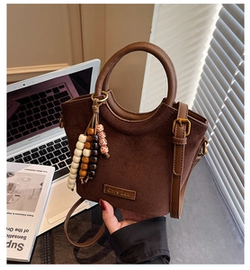 Detail of a brown suede bucket bag with round handle and colorful wooden bead charm