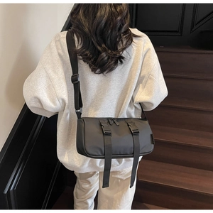 Detailed view of the black cylindrical crossbody bag with buckle straps and adjustable strap