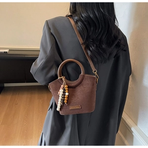 Detail of dark brown matte bucket bag with a wooden bead charm and metal logo plaque