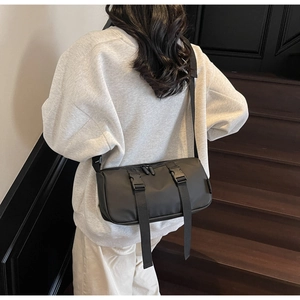 Detail of black cylinder crossbody bag with plastic buckles and top zipper closure