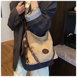 Detail of beige tote bag with leather buckle and tassel shown on grey blazer