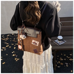 Detail of vintage brown college backpack with cartoon patches and plush doll in autumn setting