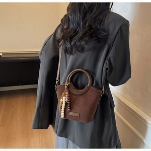 Detail of a dark brown suede bucket bag with round handles and beaded vintage charms