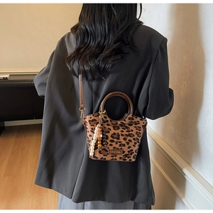 Chic leopard print crossbody bucket bag with beaded charm detail shown on a model