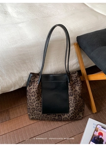 Detail view of large leopard print tote bag with black leather pockets on a wooden floor