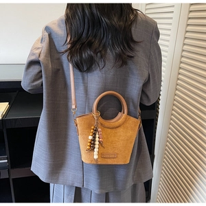 Brown suede bucket bag with round handles and beaded tassel detail on grey blazer