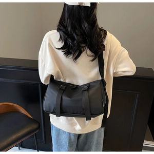 Detailed back view of a black nylon messenger bag with double buckles on a wide shoulder strap