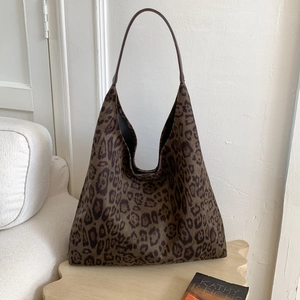 Détail d'un sac hobo à imprimé léopard posé sur un tabouret en bois dans un décor épuré