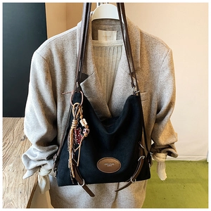 Close-up of black canvas tote bag with brown leather straps and colorful tassel detail