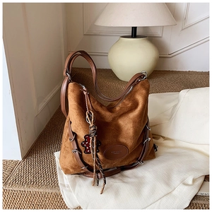 Detail showing brown suede texture, silver metal rings, and leather tassels on the hobo bag
