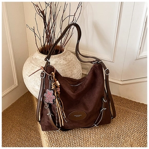 Detail of dark brown suede shoulder bag with oval logo patch and leopard bear charm