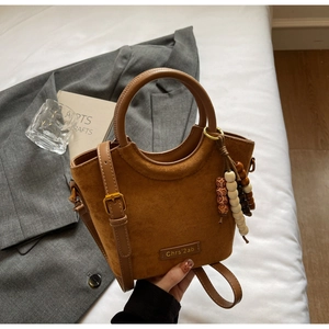 Detailed shot of brown suede crossbody bag with vintage bead charm and metal buckle handle