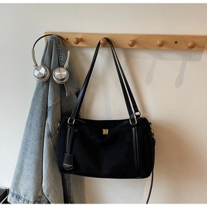 Detail of black suede tote bag with gold hardware and logo tag on a wooden hook