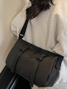 Large black utilitarian nylon crossbody bag worn over a gray hoodie by a model