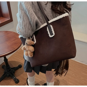 Dettaglio della borsa tote in pelle scamosciata marrone con bordo in ecopelliccia e orsetto