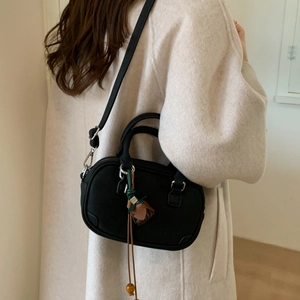 Detail of a black leather handbag featuring a vintage leaf and wooden bead charm