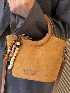 Fashionable brown suede handbag with handle and beaded charm on gray suit background