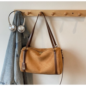 Close-up of brown suede Boston bag hanging on a hook with denim jacket and headphones