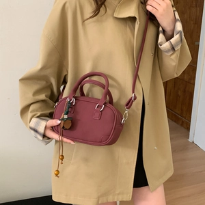Detail view of burgundy leather handbag with tassels worn on a khaki trench coat