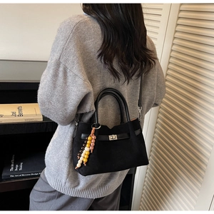 Detalle de bolso tote de ante negro con cierre giratorio plateado y colgante de cuentas