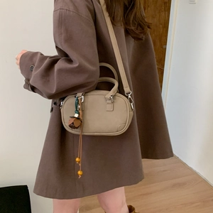 Detail view of khaki Boston bag with floral charm and adjustable strap on a brown coat