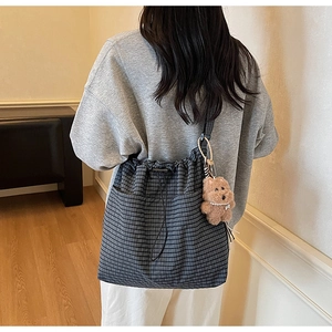 Detail of grey plaid canvas tote bag with drawstring closure and plush bear charm