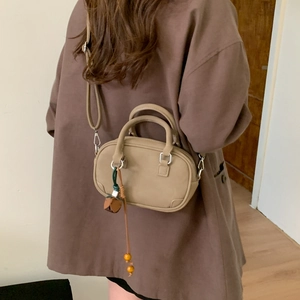 Detail view of khaki mini crossbody bag with leather and wooden bead pendant accessory