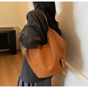 Detail shot of a large brown suede tote bag carried by a model in a gray suit