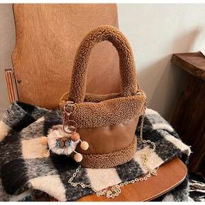 Détail d'un sac seau en peluche marron avec chaîne et charm de mouton sur une chaise