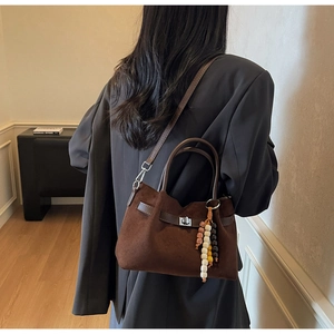 Bolso de ante marrón oscuro con cierre giratorio plateado y colgante sobre una chaqueta