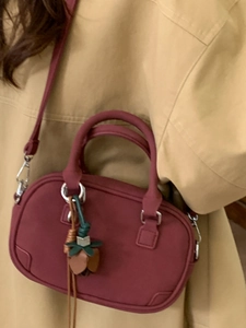 Retro burgundy shoulder bag with top handle and tulip charm on a beige trench coat