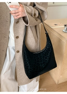 Detail of minimalist black leopard print hobo bag worn by model over a wool coat