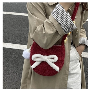 Détail d'un sac bandoulière en peluche bordeaux avec nœud blanc porté sur trench kaki