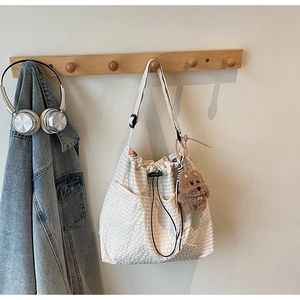 Detail of cream canvas tote bag with grid texture, drawstring closure and dog plush charm
