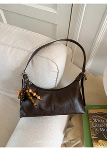 Detail der dunkelbraunen Retro-Baguette-Tasche mit Holzperlenanhänger auf Textur